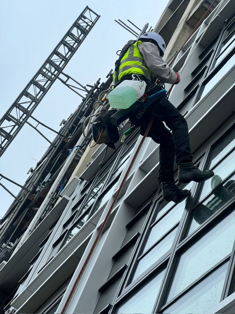 Window Cleaning After Construction – A abseiled window cleaner polishing windows